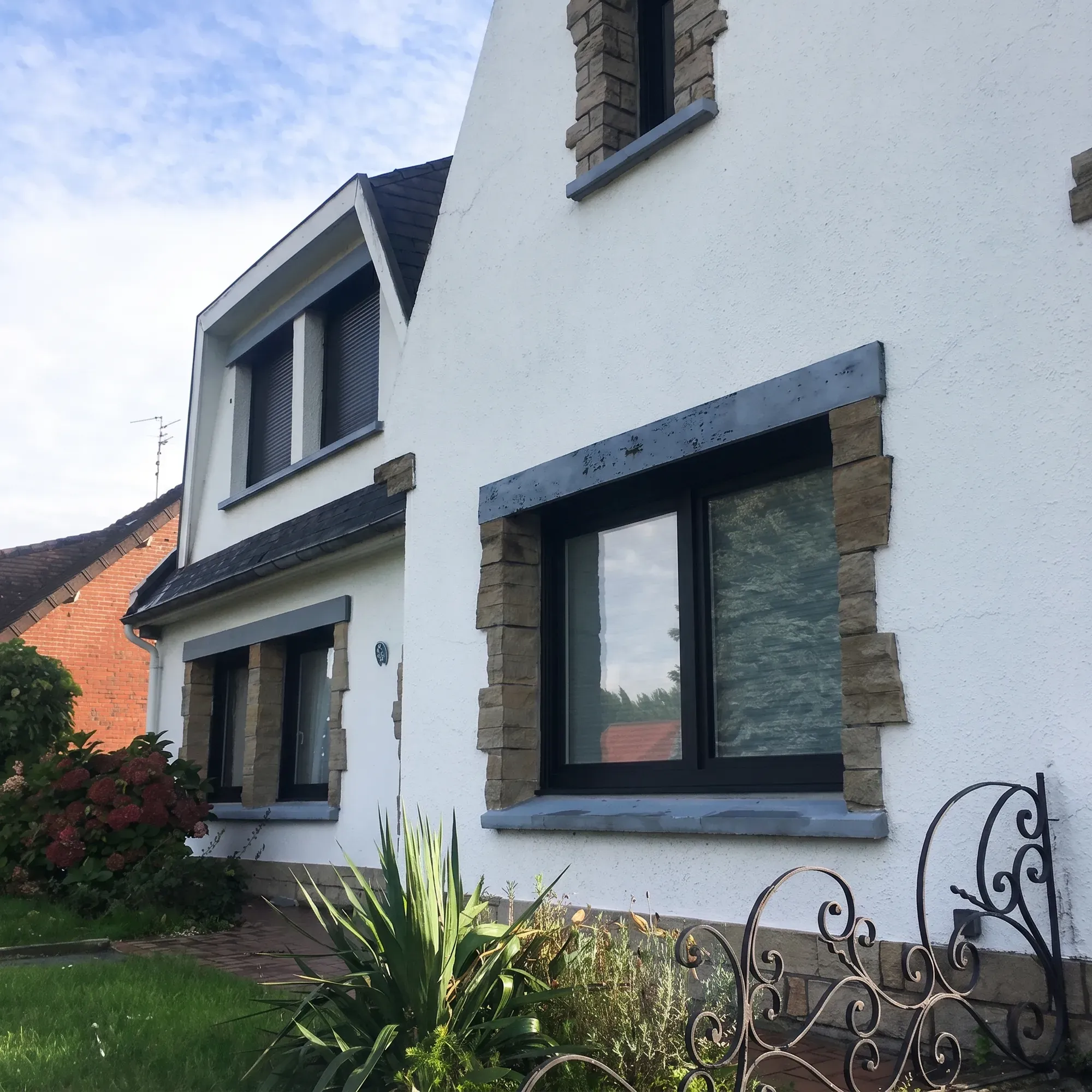 Fenêtre hybride 76 anthracite avec encadrement en pierre sur une maison blanche