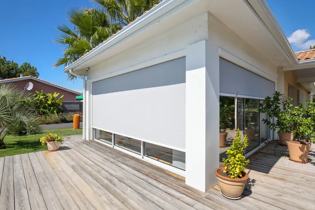 Store screen extérieur gris descendu sur une baie d'angle, terrasse d'une maison contemporaine
