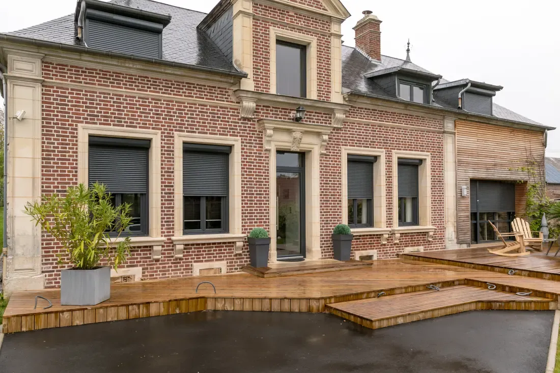 Maison en brique équipée de volets roulants extérieurs anthracite, avec terrasse en bois