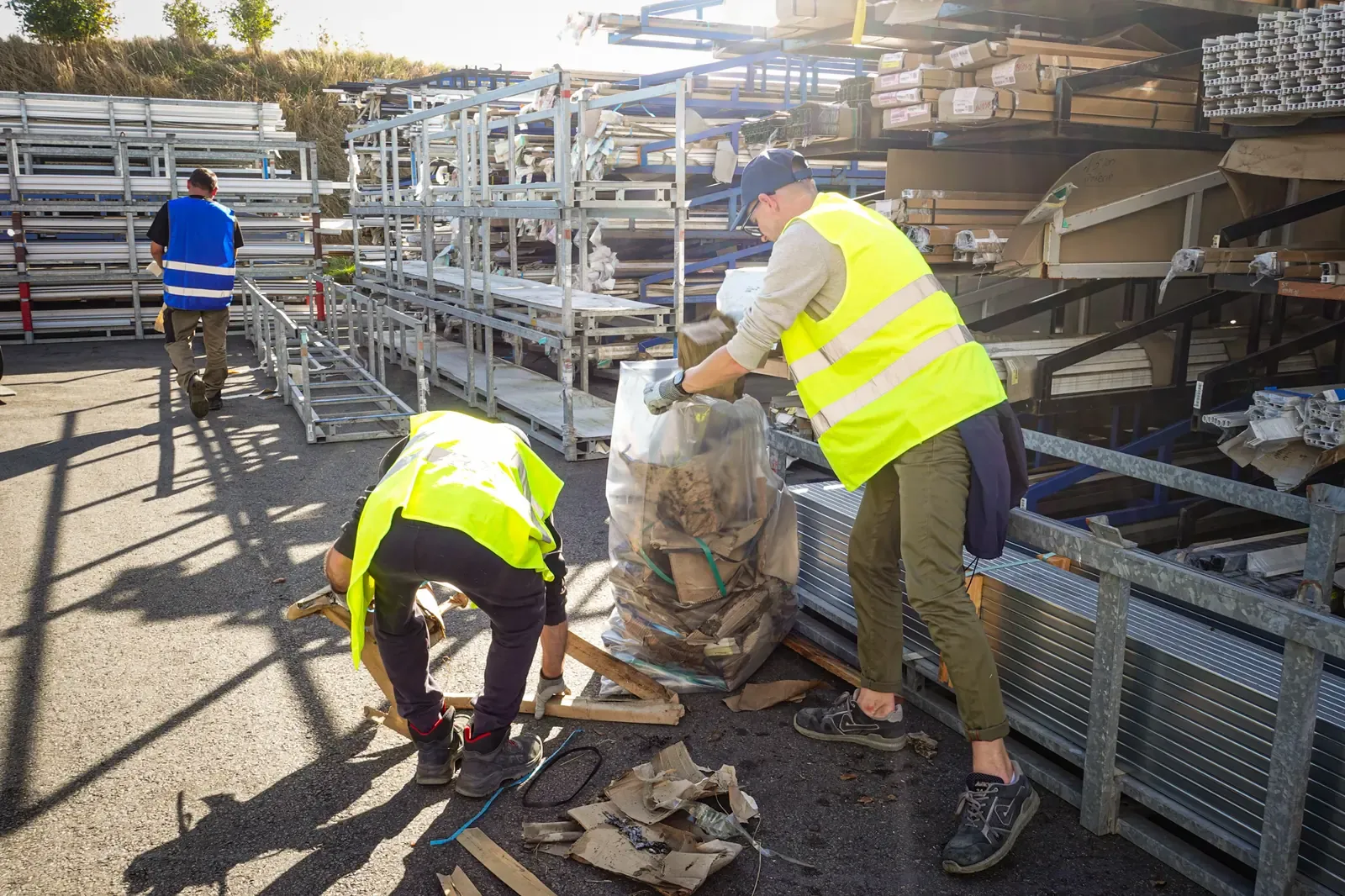Deux collaborateurs ramassent des déchets entre les racks de stockage de profilés, sur le site de Douvrin
